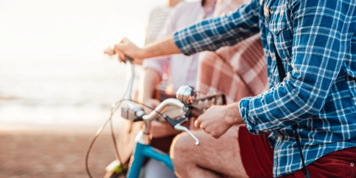 Mann in kurzer Hose und Hemd sitzt auf Fahrrad und genießt Freizeit am Strand.