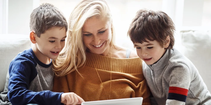 Mutter und zwei Kinder schauen gemeinsam auf Tablet.
