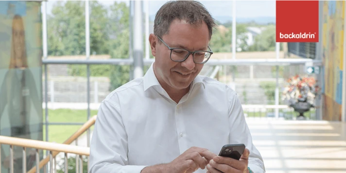 Backaldrin CEO steht in Stiegenaufgang und schaut auf sein Smartphone.