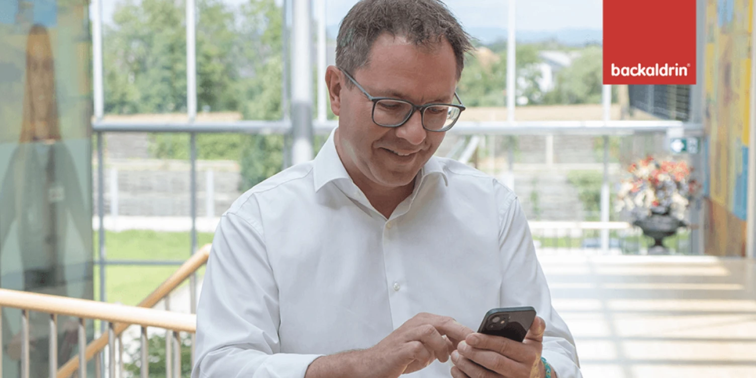 Backaldrin CEO steht in Stiegenaufgang und schaut auf sein Smartphone.