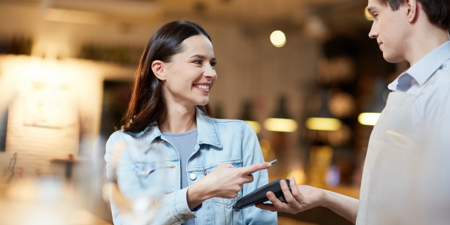 Frau bezahlt per App und Smartphone in einem Lokal.