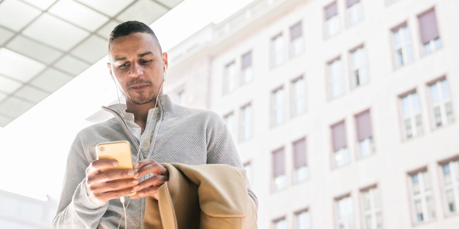 Mann steht im Freien und schaut auf sein Smartphone.