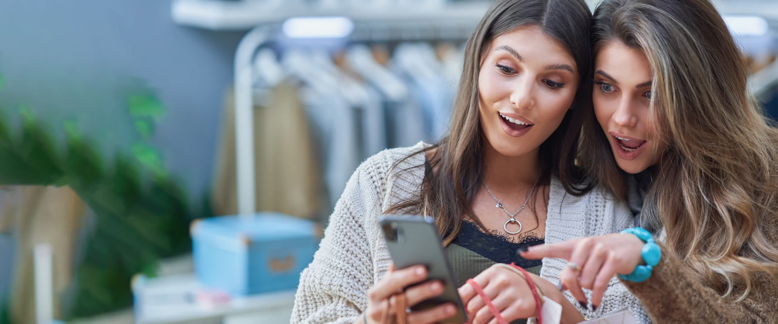 Zwei Frauen, die freudig erstaunt darüber sind, was sie auf einem Smartphone sehen.