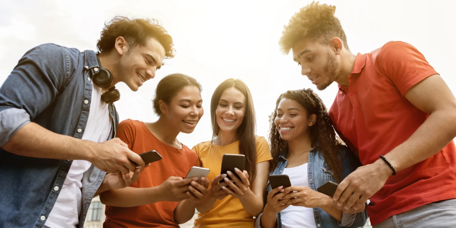 Gruppe junger fröhlicher Menschen schaut gemeinsam auf ihre Smartphones.