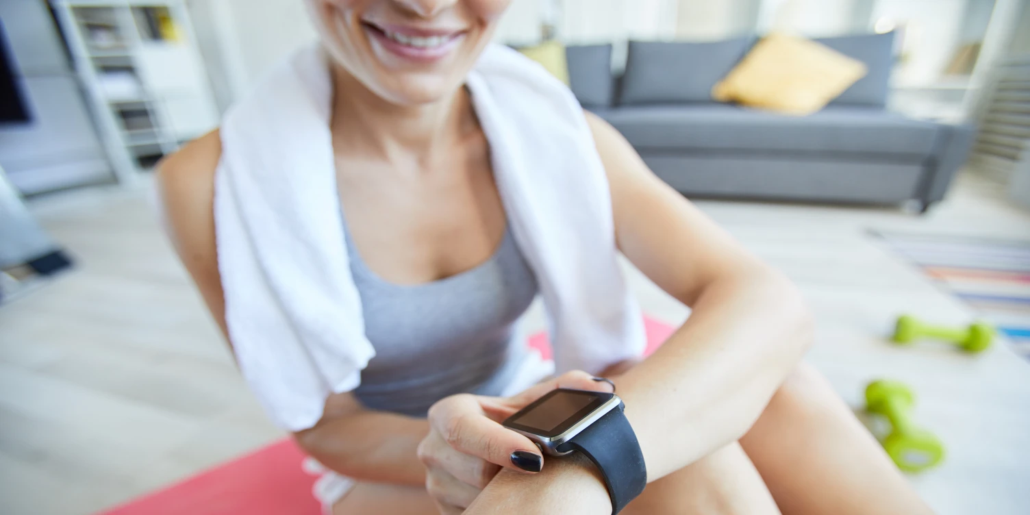 Frau in Fitness-Outfit drückt auf die Smartwatch an ihrem Handgelenk.