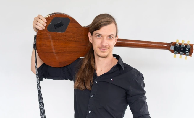 Employee Thomas Urbanitsch carries a guitar on his shoulder.