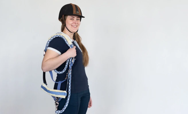 Employee Viktoria Lang wears a riding helmet and carries a bridle on her shoulder.