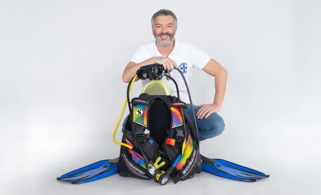 CEO Wolfgang Stockner kneels behind diving equipment.