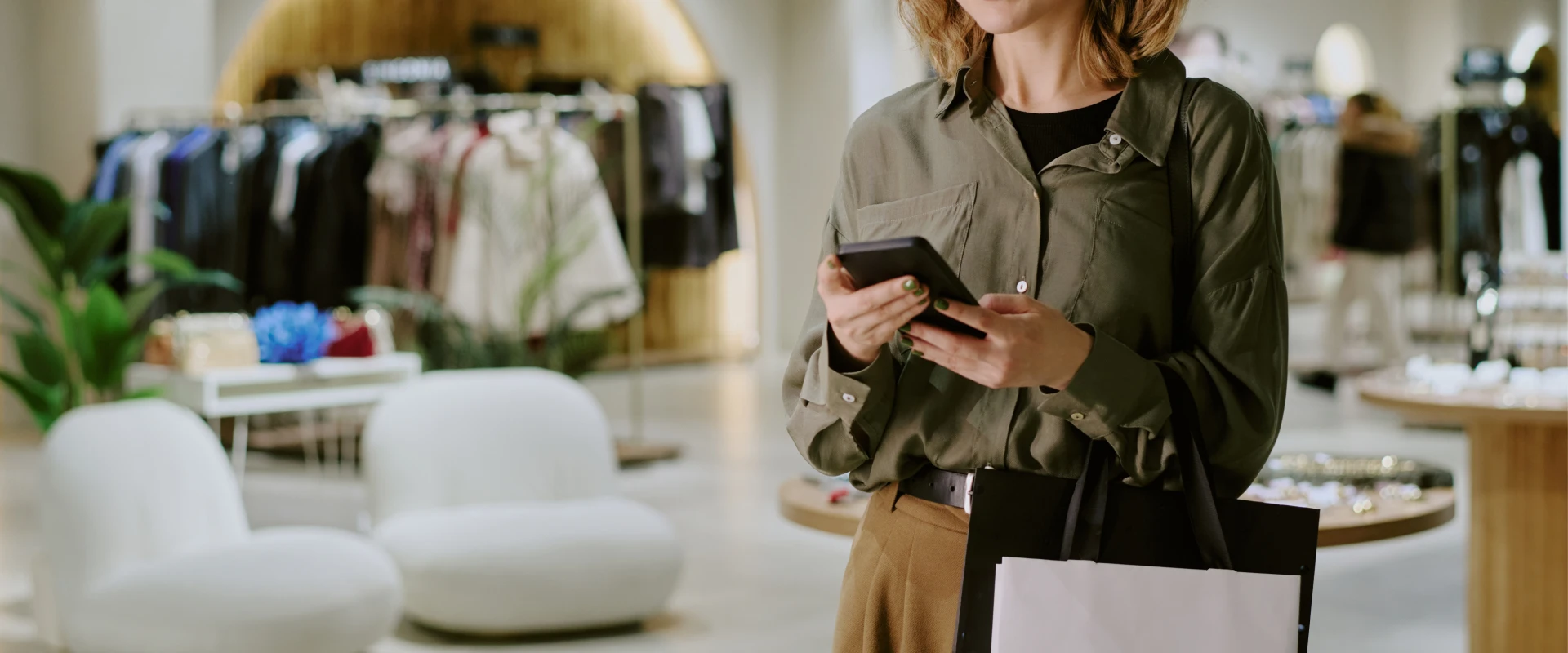 Frauen beim Einkaufen in einem Bekleidungsladen die auf ihr Smartphone sieht.