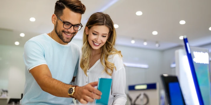 Junges Paar schaut sich in Geschäft ein neues Smartphone an.