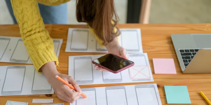 Frau plant mit Blick auf Smartphone die Screens einer neuen App.