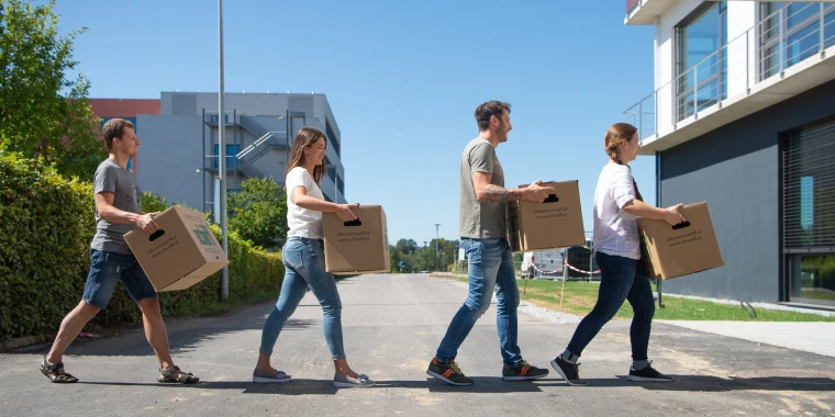 Mitarbeiter*innen tragen Umzugskartons über die Straße in neues Büro.