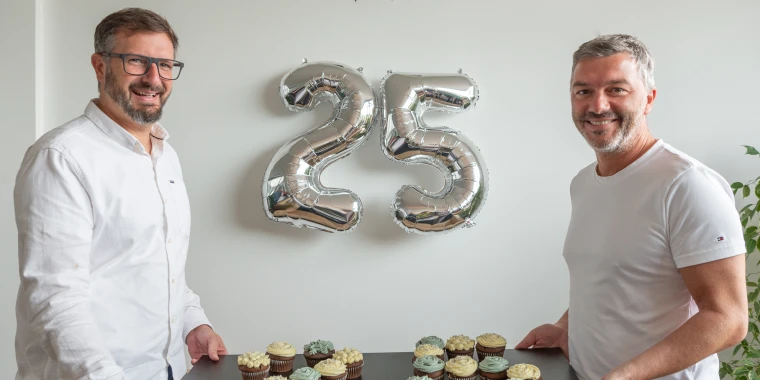 Roland Sprengseis and Wolfgang Stockner in front of silver balloons showing the number 25.