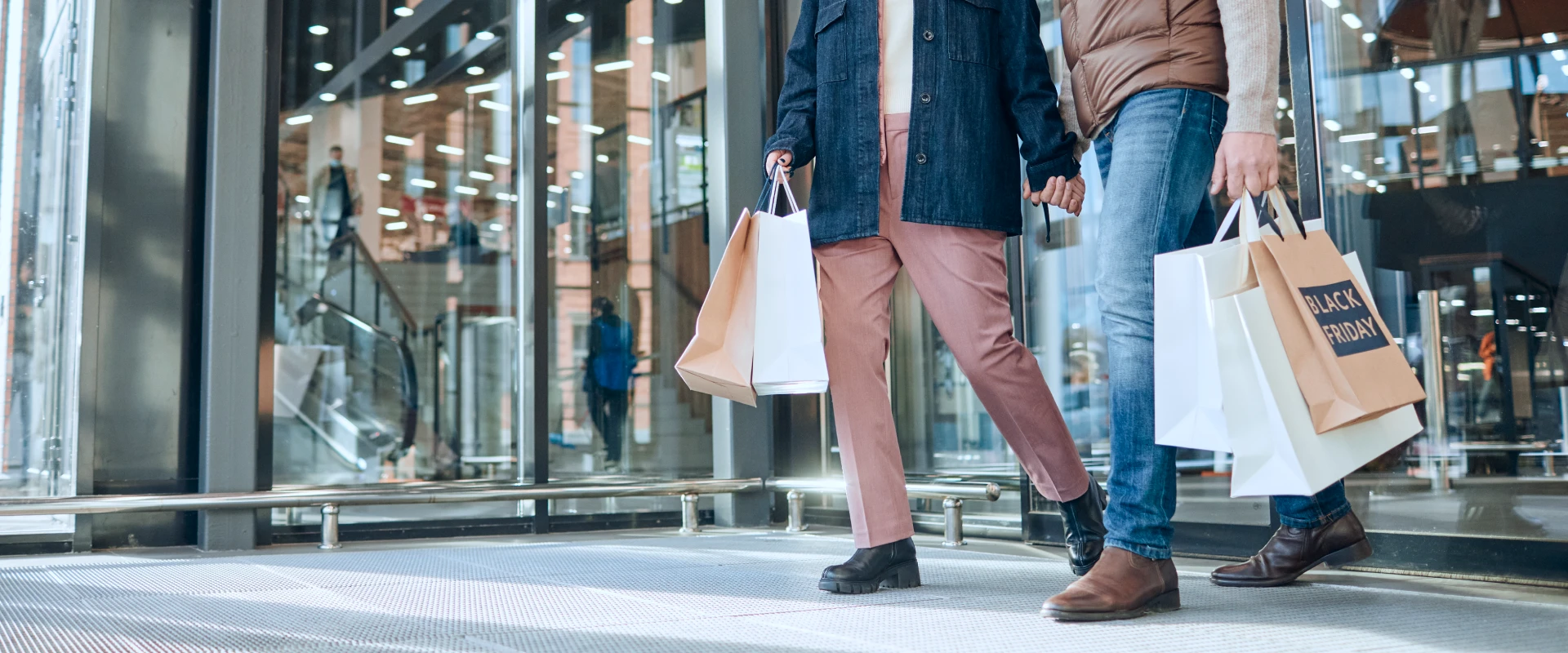 Paar verlässt Shoppingcenter mit mehreren Einkaufstaschen in den Händen.