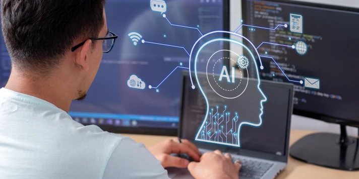 A man sits in front of a laptop and two screens and works on AI.