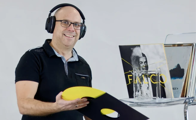 Employee Stefan Kumpfmüller wears headphones and holds a record.