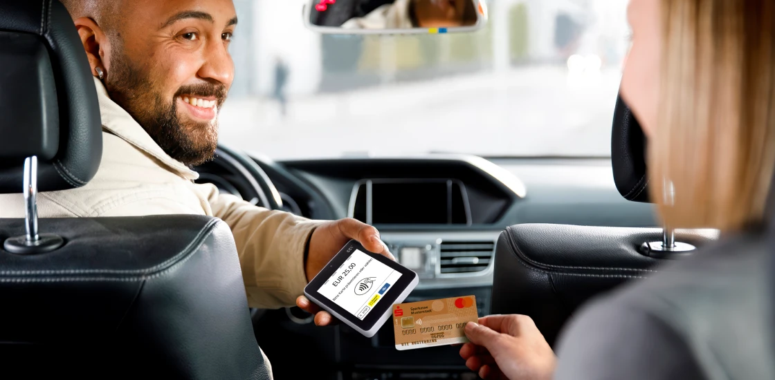 Kundin bezahlt im Taxi kontaktlos mit Sparkasse-Karte, Fahrer hält mobiles Kartenlesegerät und lächelt.