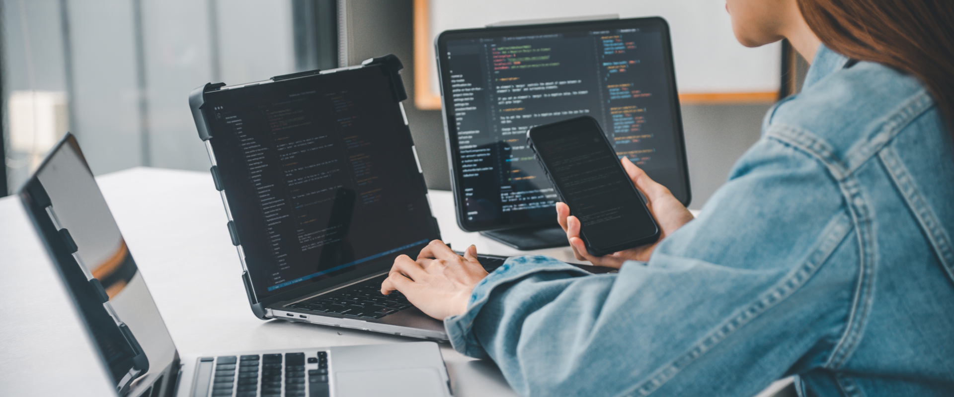 Developer in front of multiple screens with code and a smartphone – illustration of technologies and programming languages used in software development at bluesource.