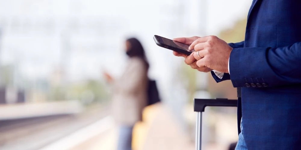 Geschäftsmann am Bahnhof nutzt Mobile Banking Services auf seinem Smartphone, um unterwegs Transaktionen zu prüfen.