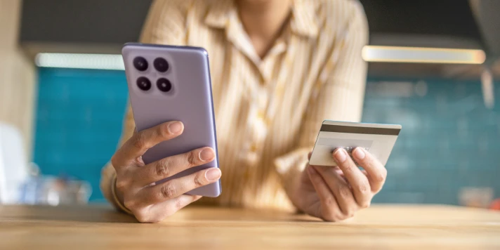 Frau hält Smartphone in einer und Kreditkarte in der anderen Hand beim Barrierefreiheits-Check von Banking Apps