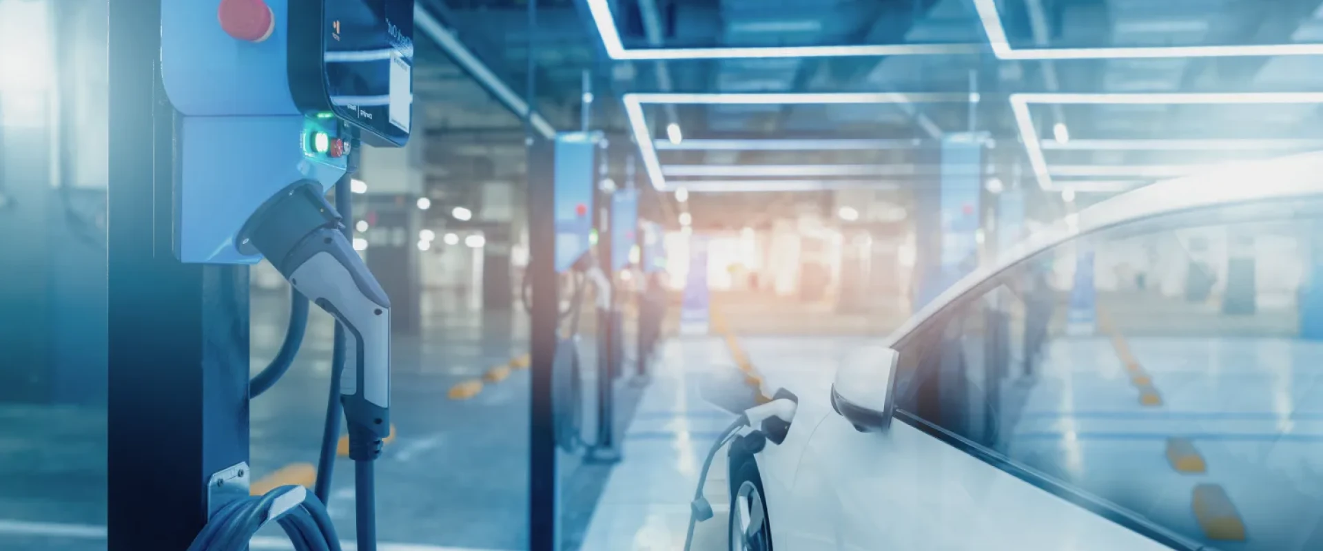 Innenansicht eines modernen Parkhauses mit mehreren Ladestationen für Elektroautos. Ein weißes E-Auto ist im Vordergrund an eine Ladestation angeschlossen.
