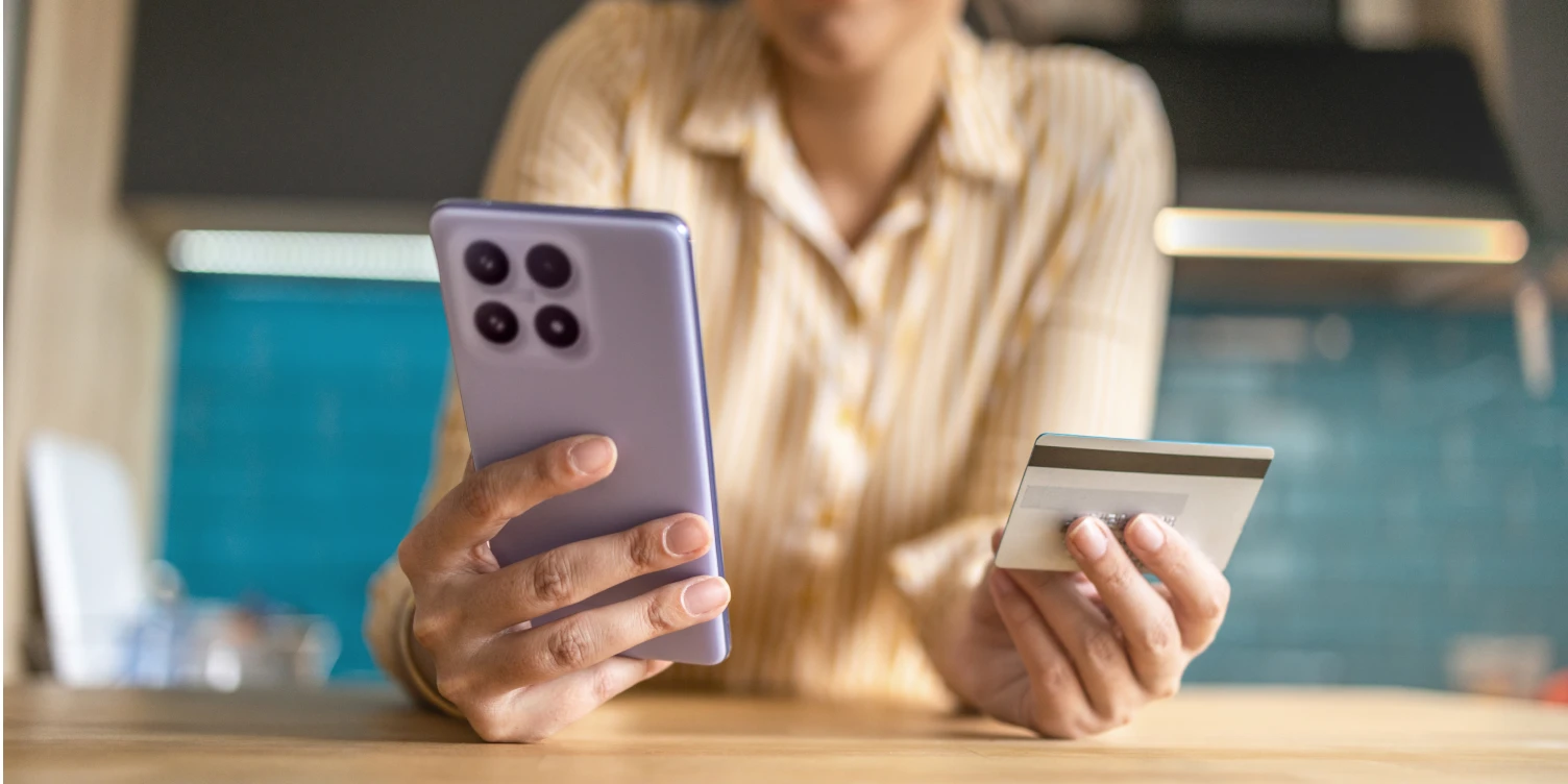 Frau hält Smartphone in einer und Kreditkarte in der anderen Hand beim Barrierefreiheits-Check von Banking Apps